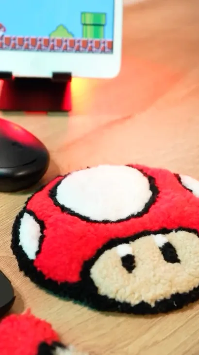 Portavasos de tufting con forma de hongo rojo de Mario Bros sobre un escritorio de madera